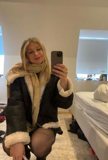 Dara Greig in a cozy coat and scarf taking a mirror selfie.